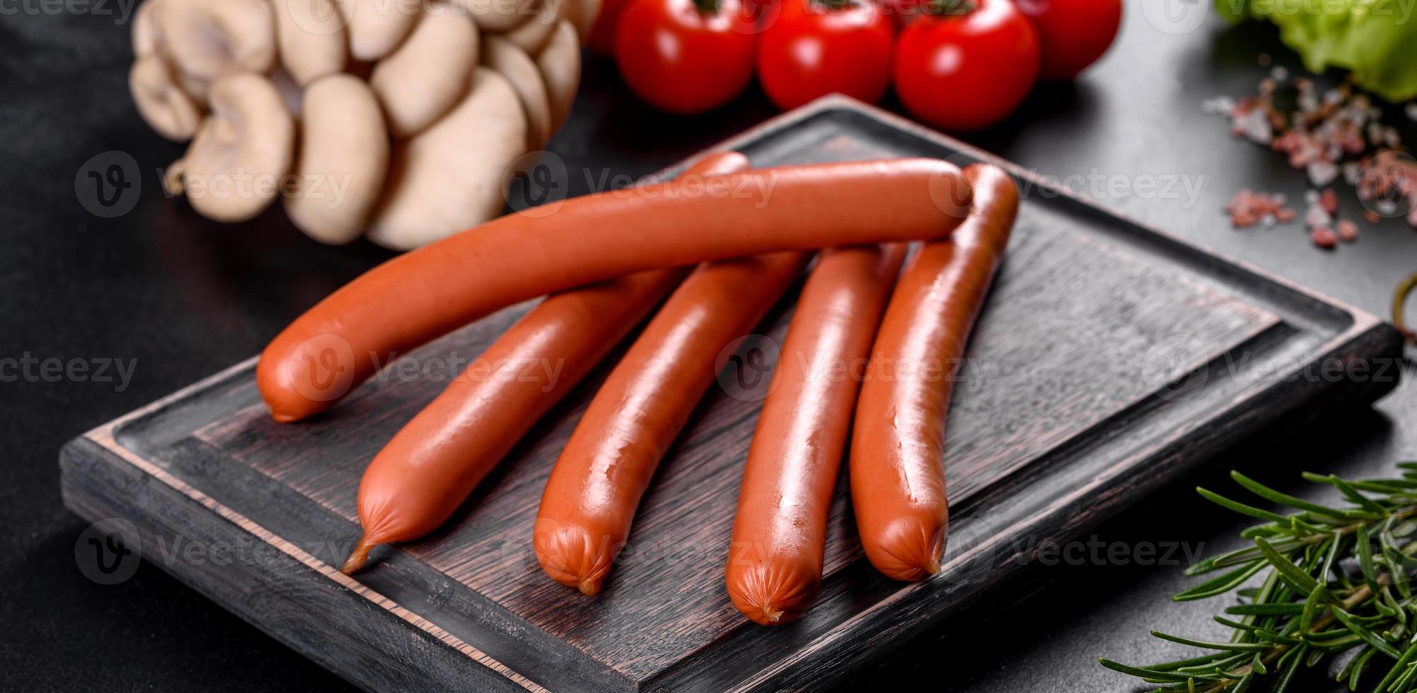 Boiled sausages on a wooden cutting board on a dark concrete background photo