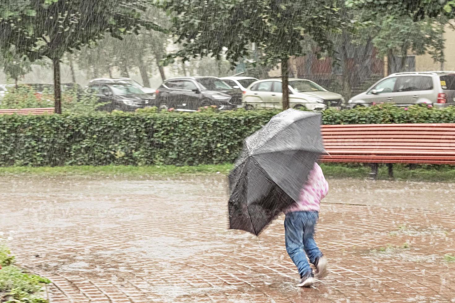 A little girl is having fun running around with an umbrella in the heavy rain photo