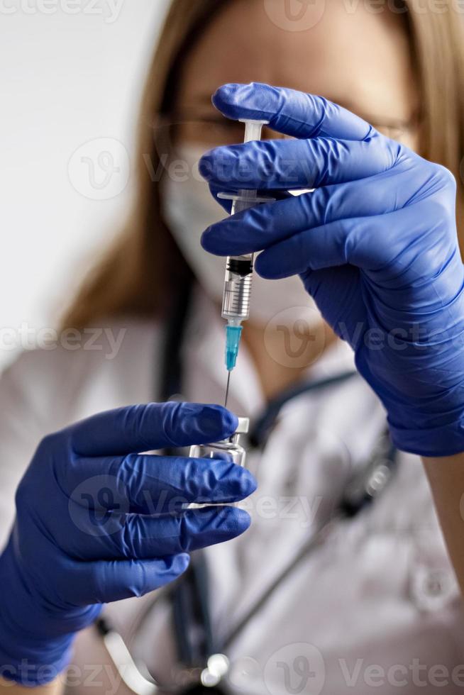 A female doctor wearing a medical mask draws the coronavirus vaccine into a syringe photo