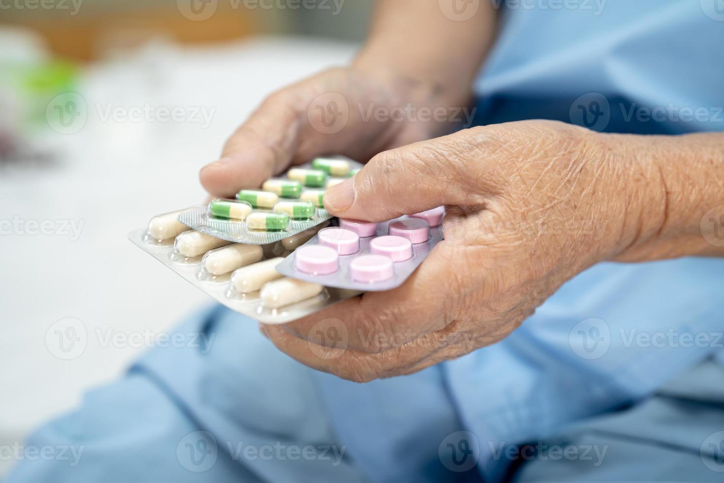 Asian senior or elderly old lady woman patient holding antibiotics capsule pills in blister packaging for treatment infection patient in hospital Pharmacy drugstore concept. photo