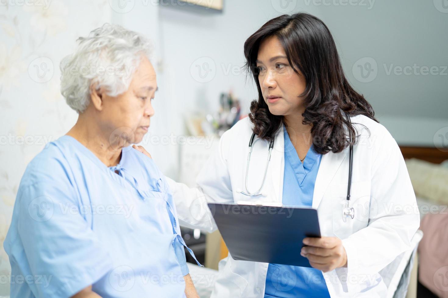 Doctor talking about diagnosis and note on clipboard with Asian senior or elderly old lady woman while lying on bed in nursing hospital ward, healthy strong medical concept. photo