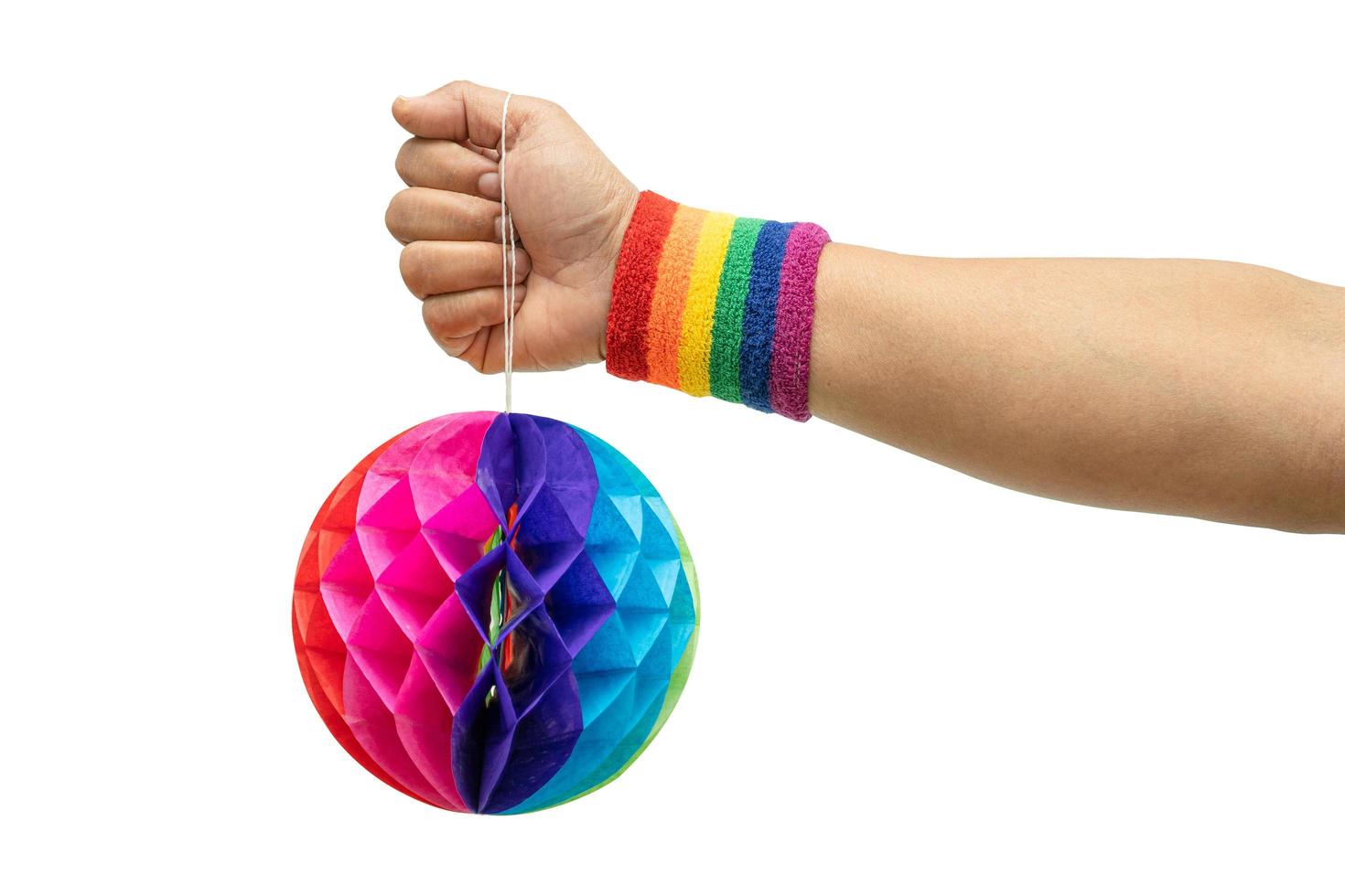 Asian lady wearing rainbow flag wristbands holding colorful honeycomb paper flowers ball isolate on white background with clipping path, symbol of LGBT pride month. photo