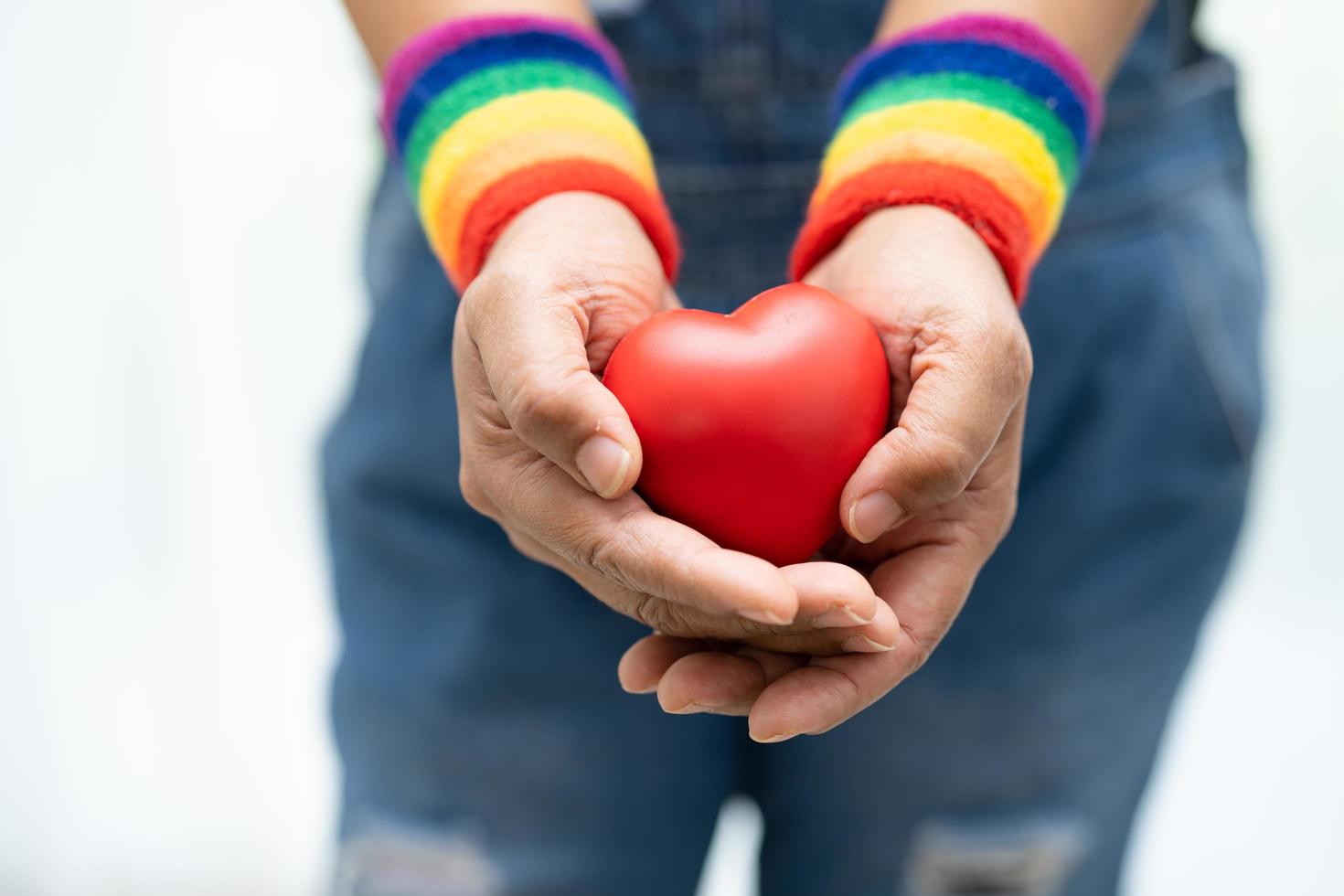 Asian lady wearing rainbow flag wristbands and hold red heart, symbol of LGBT pride month celebrate annual in June social of gay, lesbian, bisexual, transgender, human rights. photo