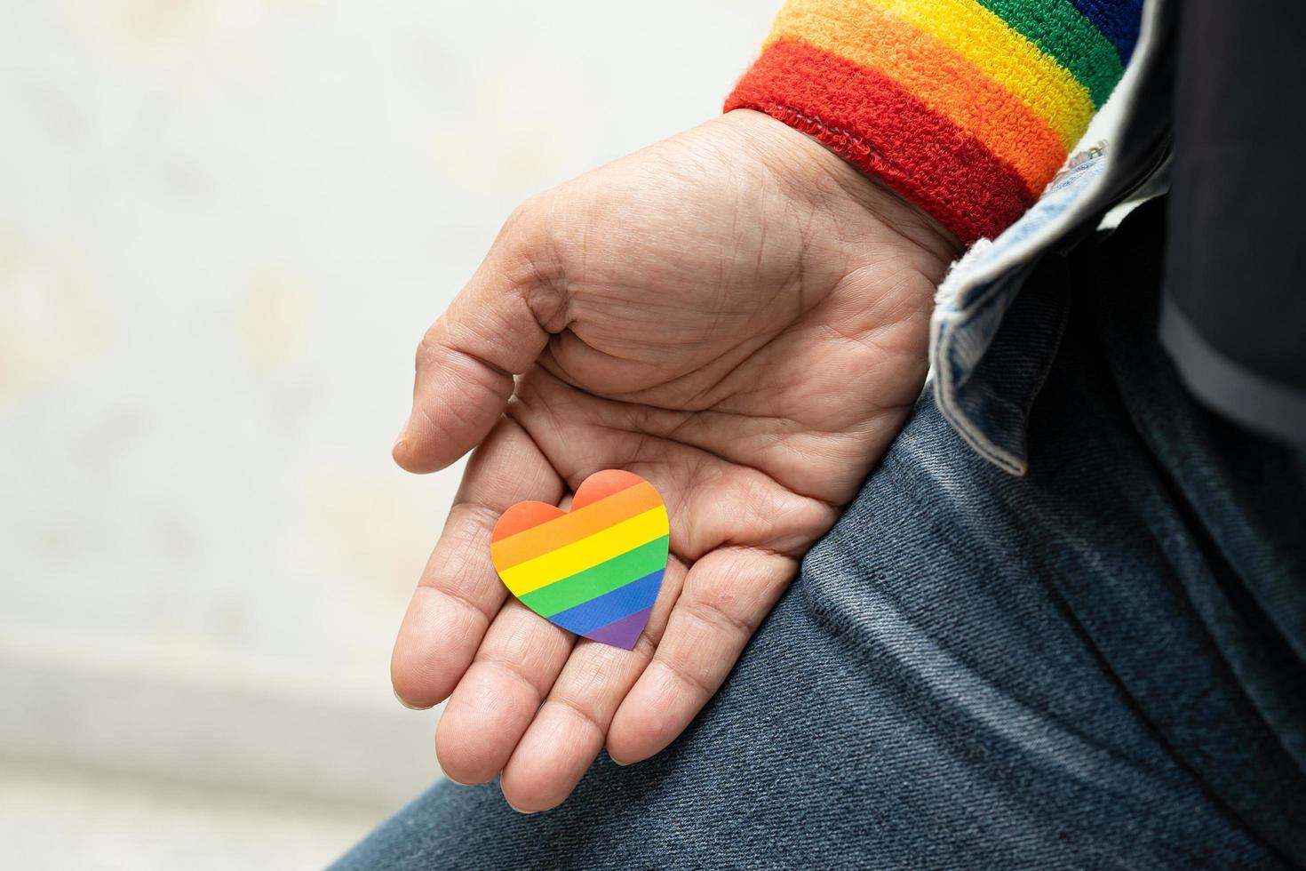 Asian lady wearing blue jean jacket or denim shirt and holding rainbow color flag heart, symbol of LGBT pride month celebrate annual in June social of gay, lesbian, bisexual, transgender, human rights. photo