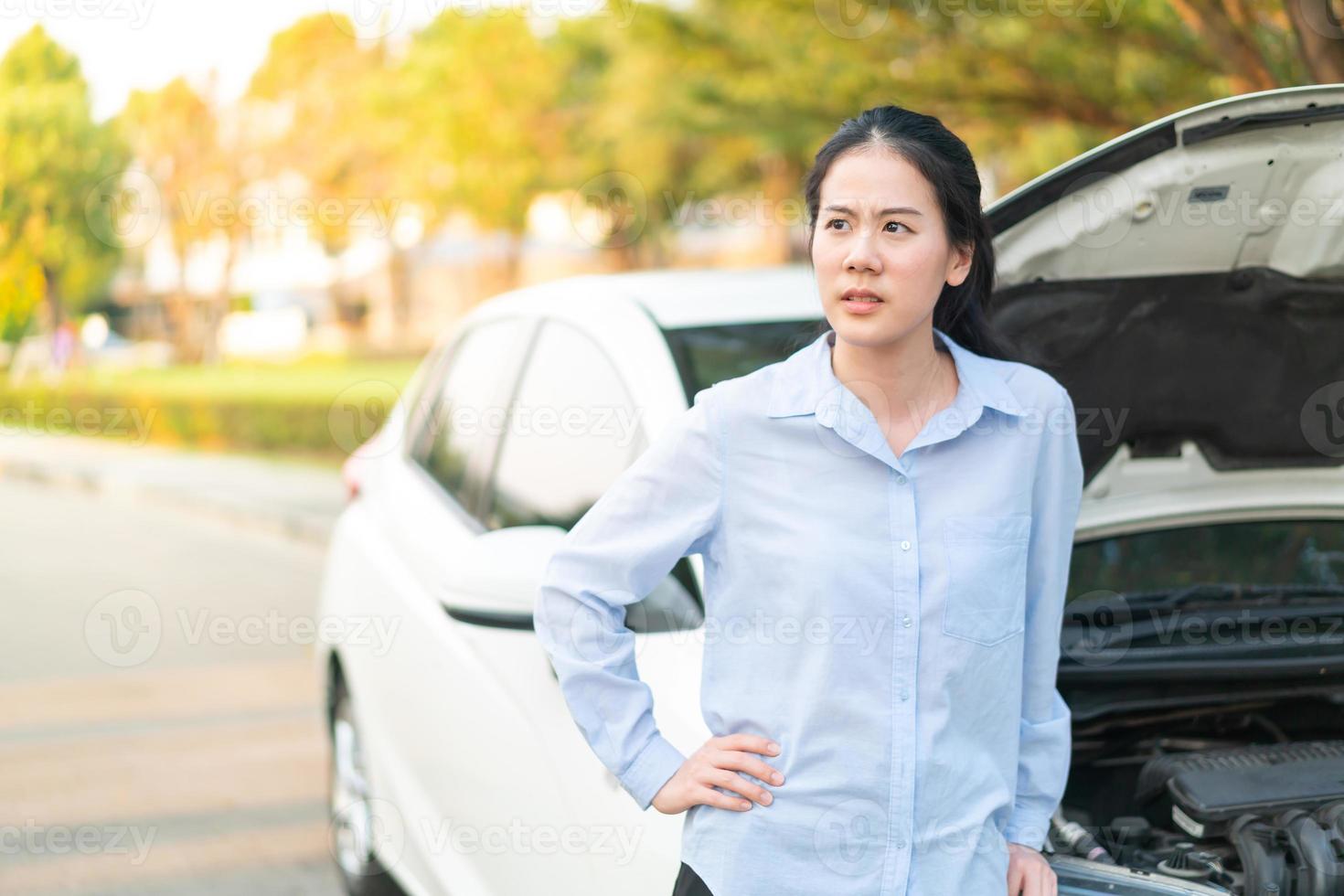 Mujer joven de pie cerca del coche averiado con el capó levantado que tiene problemas con su vehículo foto