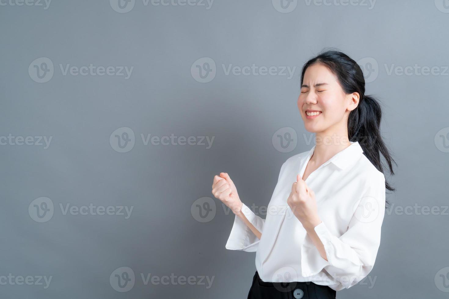 Asian woman rejoicing her success and victory clenching her fists with joy. Lucky woman being happy to achieve her aim and goals. Positive emotions, feelings. photo