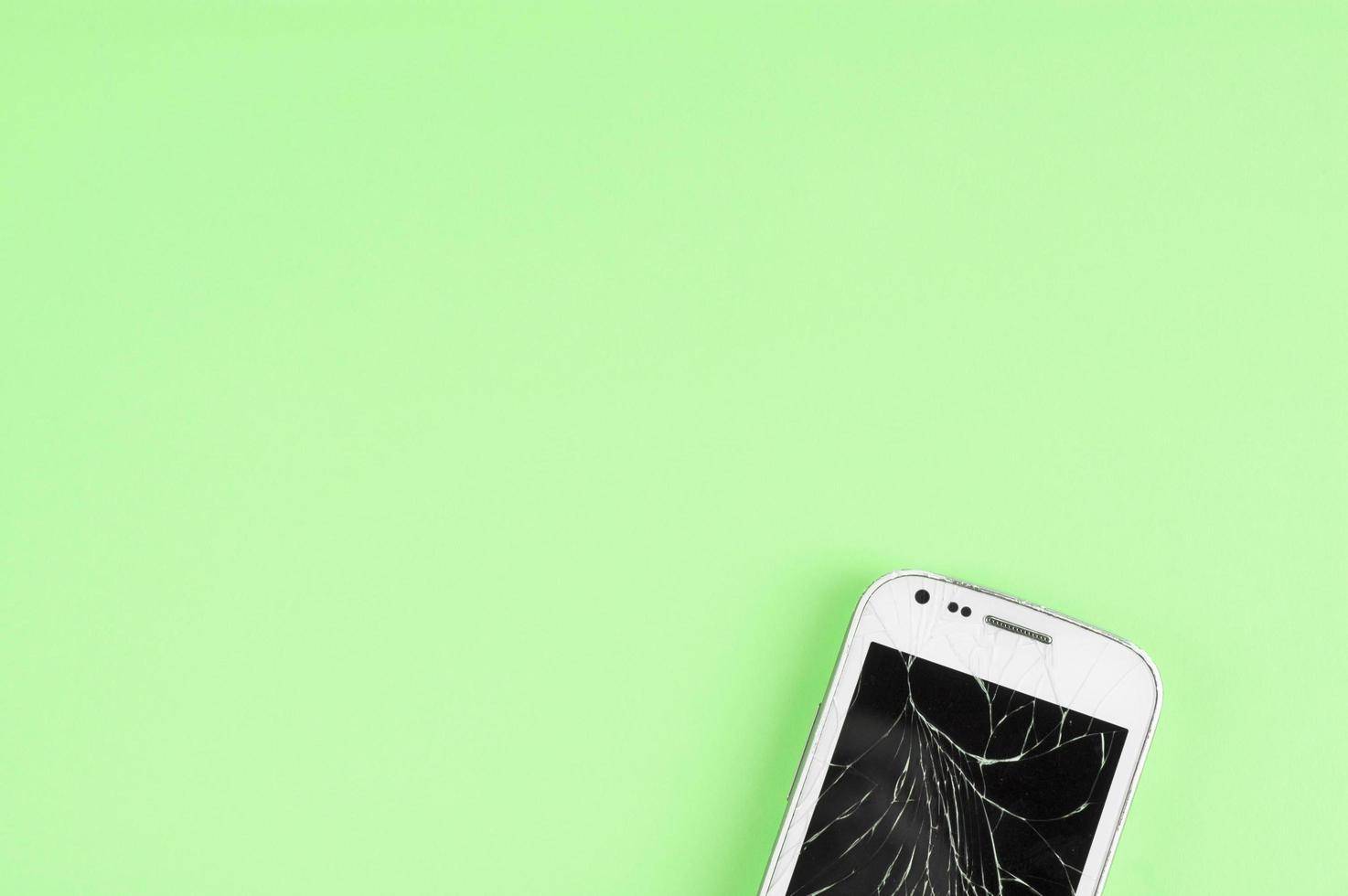 A broken touchscreen cell phone on green background with copy space for text photo