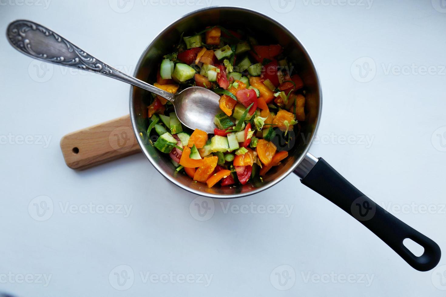 Ensalada de verduras de temporada de verano en una cacerola con una cuchara foto