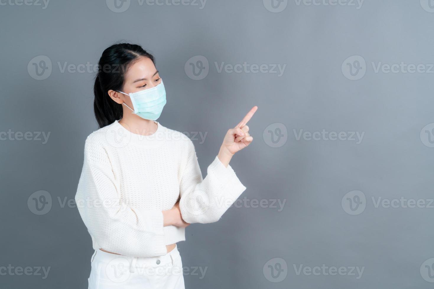 Joven asiática vistiendo mascarilla médica y señalar con el dedo foto