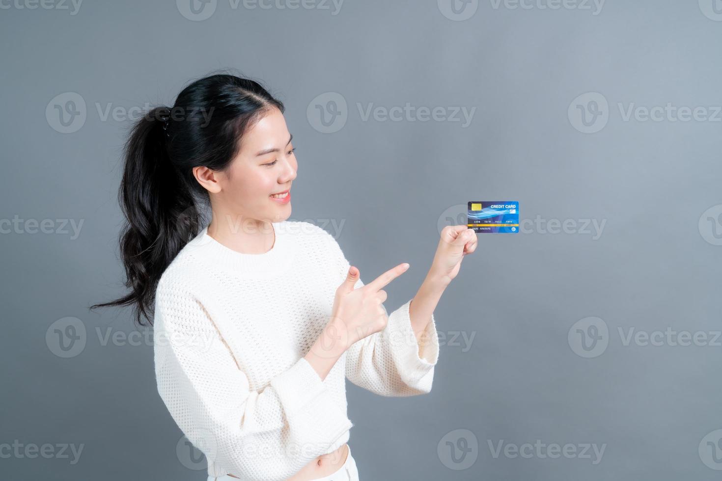 Retrato de una hermosa joven asiática en suéter mostrando tarjeta de crédito con espacio de copia foto