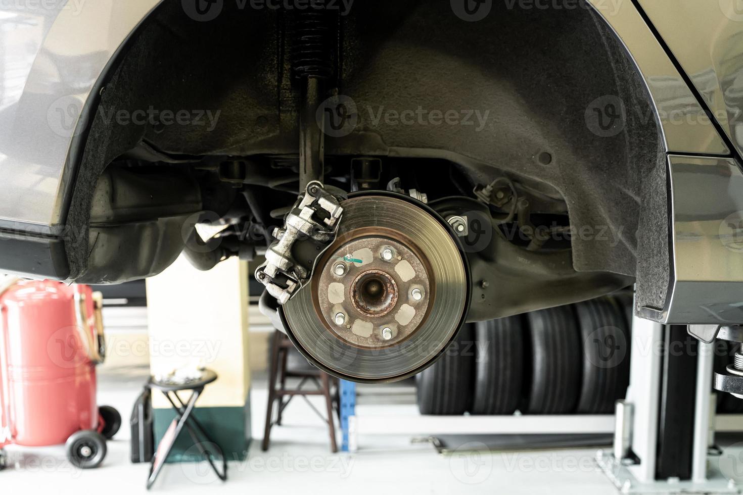 Coche de disco de cerca - mecánico desenroscando piezas de automóvil mientras trabaja bajo un auto levantado foto