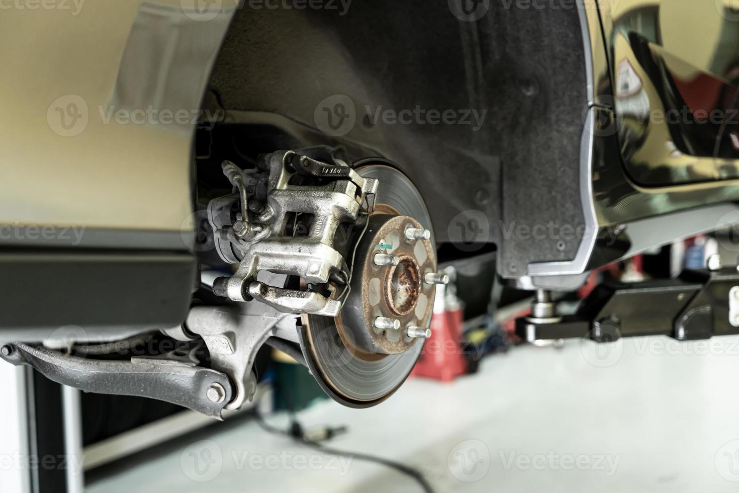 Disc car close up - mechanic unscrewing automobile parts while working under a lifted auto photo