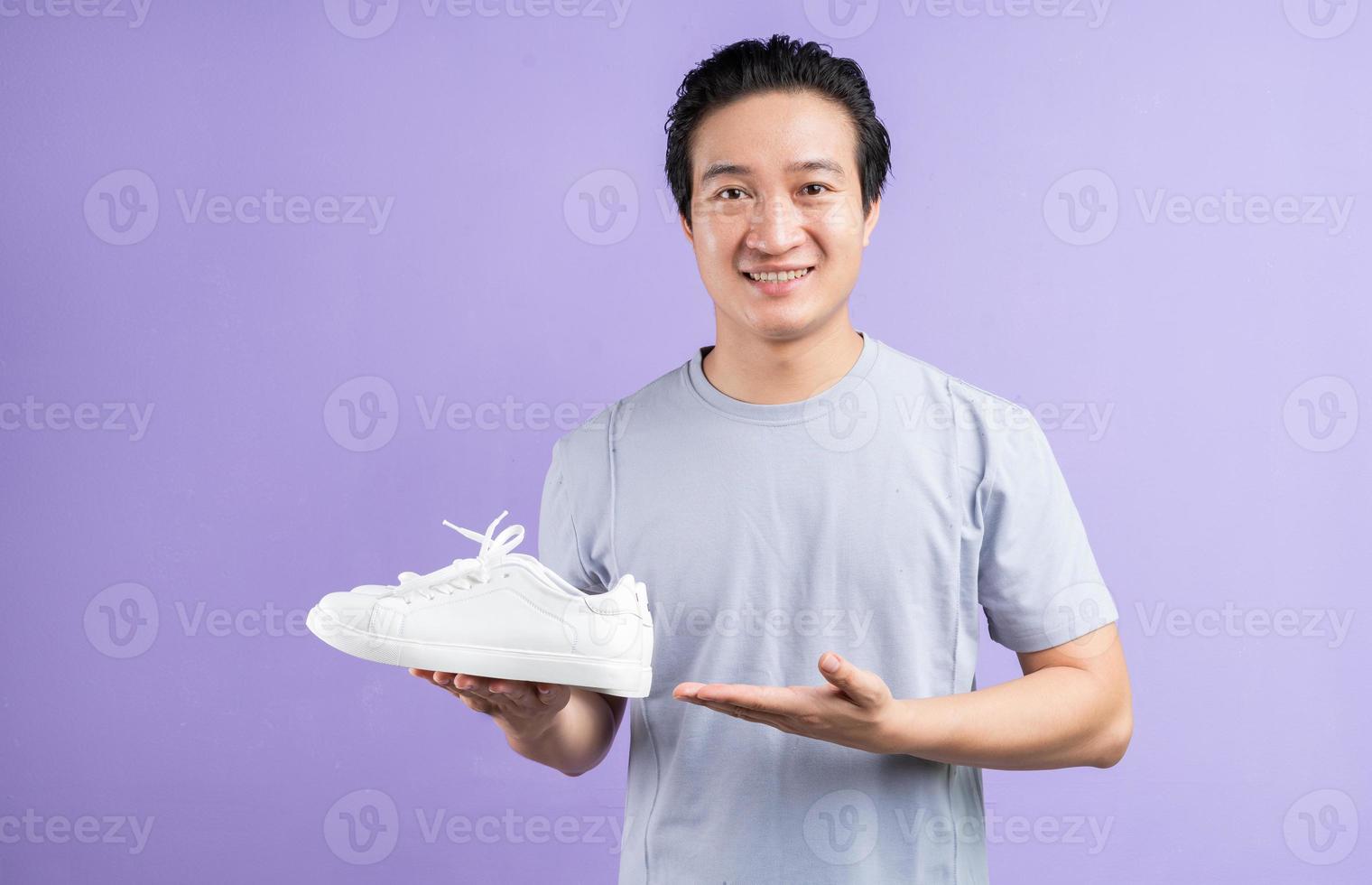 hombre asiático, tenencia, zapatillas de deporte, en, fondo púrpura foto
