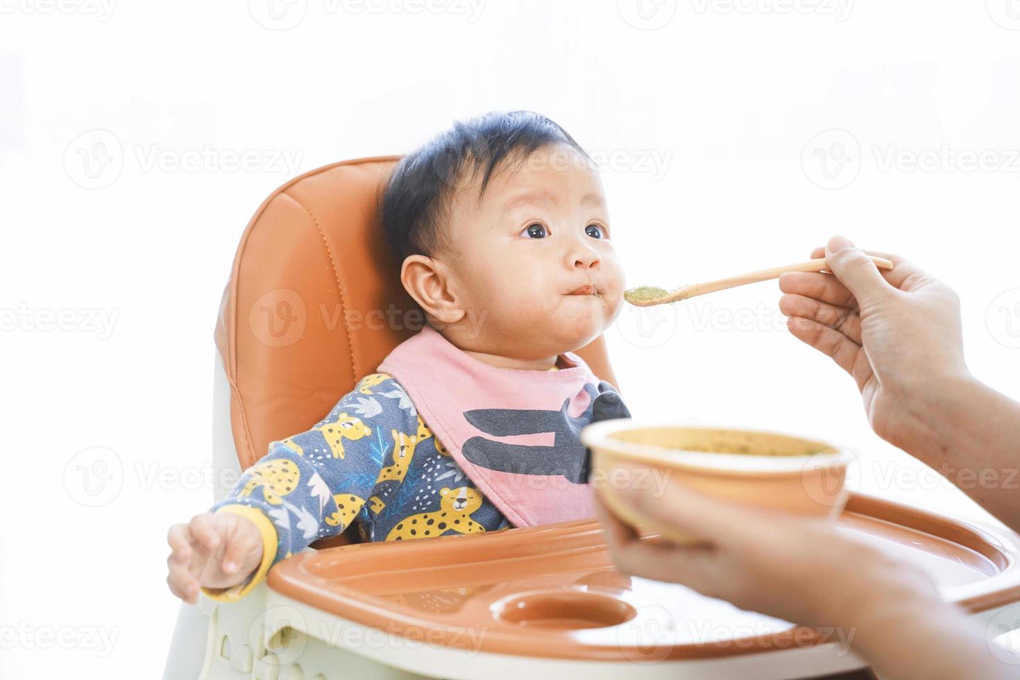 Niña de 6 meses comiendo alimentos mezclados en una silla alta. foto