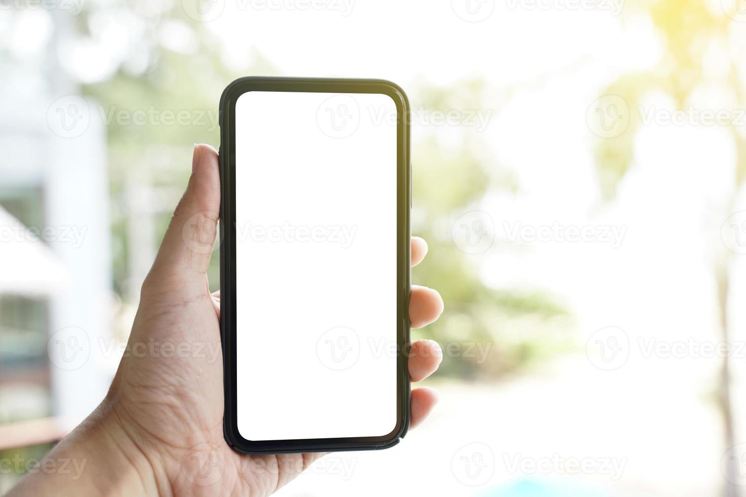 maqueta de teléfono móvil de pantalla en blanco. Mano de hombre sosteniendo y usando un teléfono móvil con pantalla blanca en blanco contra el bokeh del fondo de la naturaleza. foto