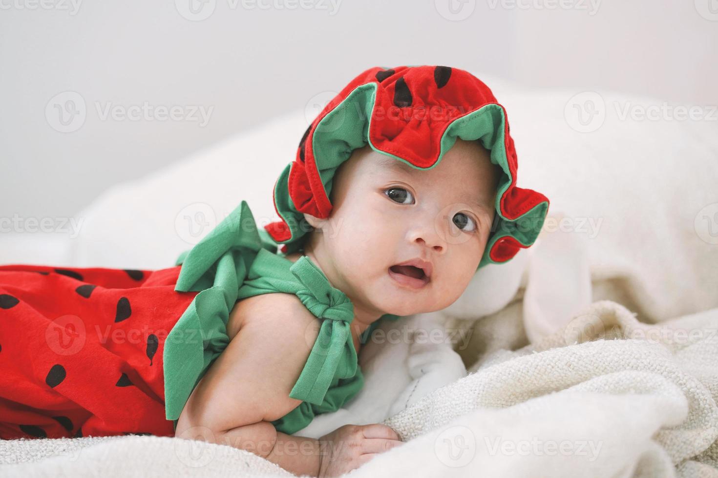 lindo bebé está acostado boca abajo en la cama y vistiendo un traje de fresa. foto