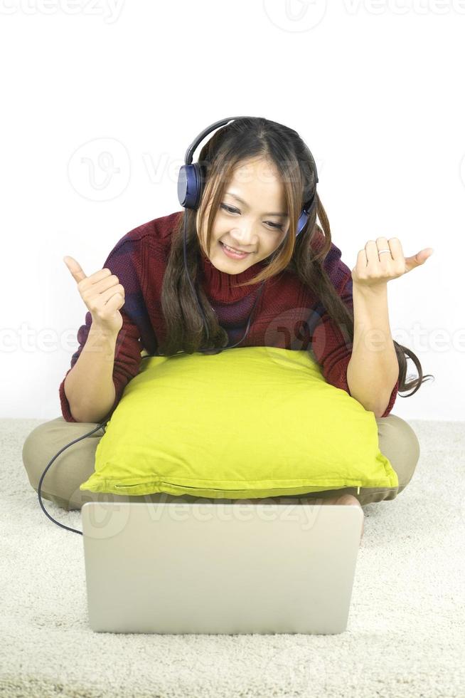 hermoso retrato joven mujer asiática sentada en el suelo con ordenador portátil y auriculares sobre fondo blanco. foto