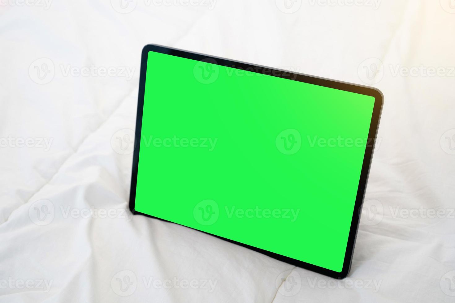 Top view of black tablet on a bed with green chroma key. photo