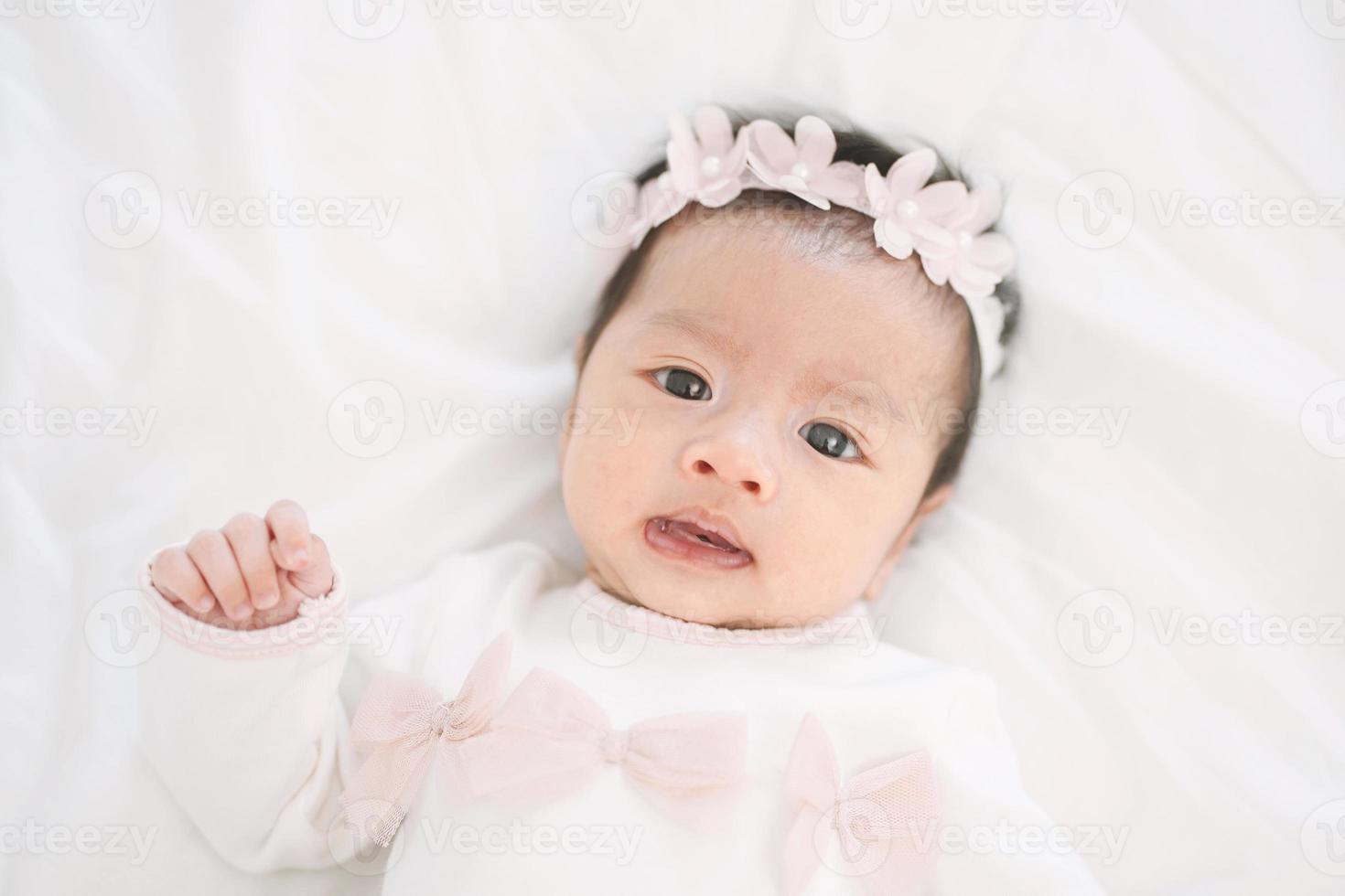 Adorable little baby girl in a beautiful dress with flower band lying on a white blanket. photo