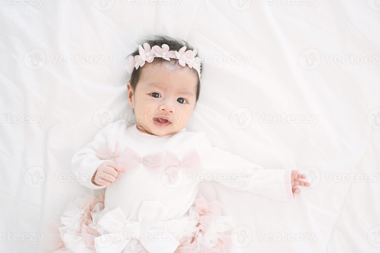 adorable niña en un hermoso vestido con banda de flores acostado sobre una manta blanca. foto