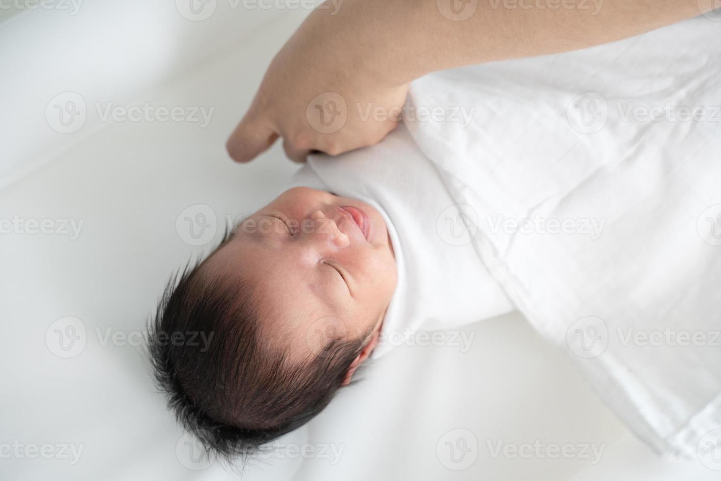 New born baby smiling while mother's hand swaddling her body with white blanket. photo