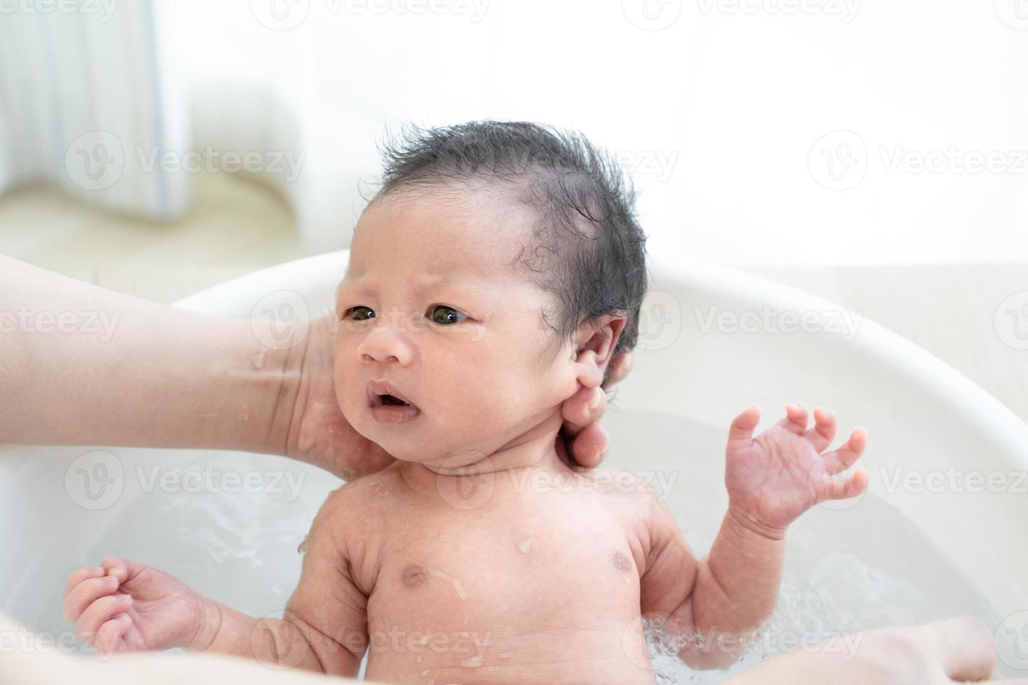 El recién nacido está siendo bañado por su madre usando una tina en casa. foto