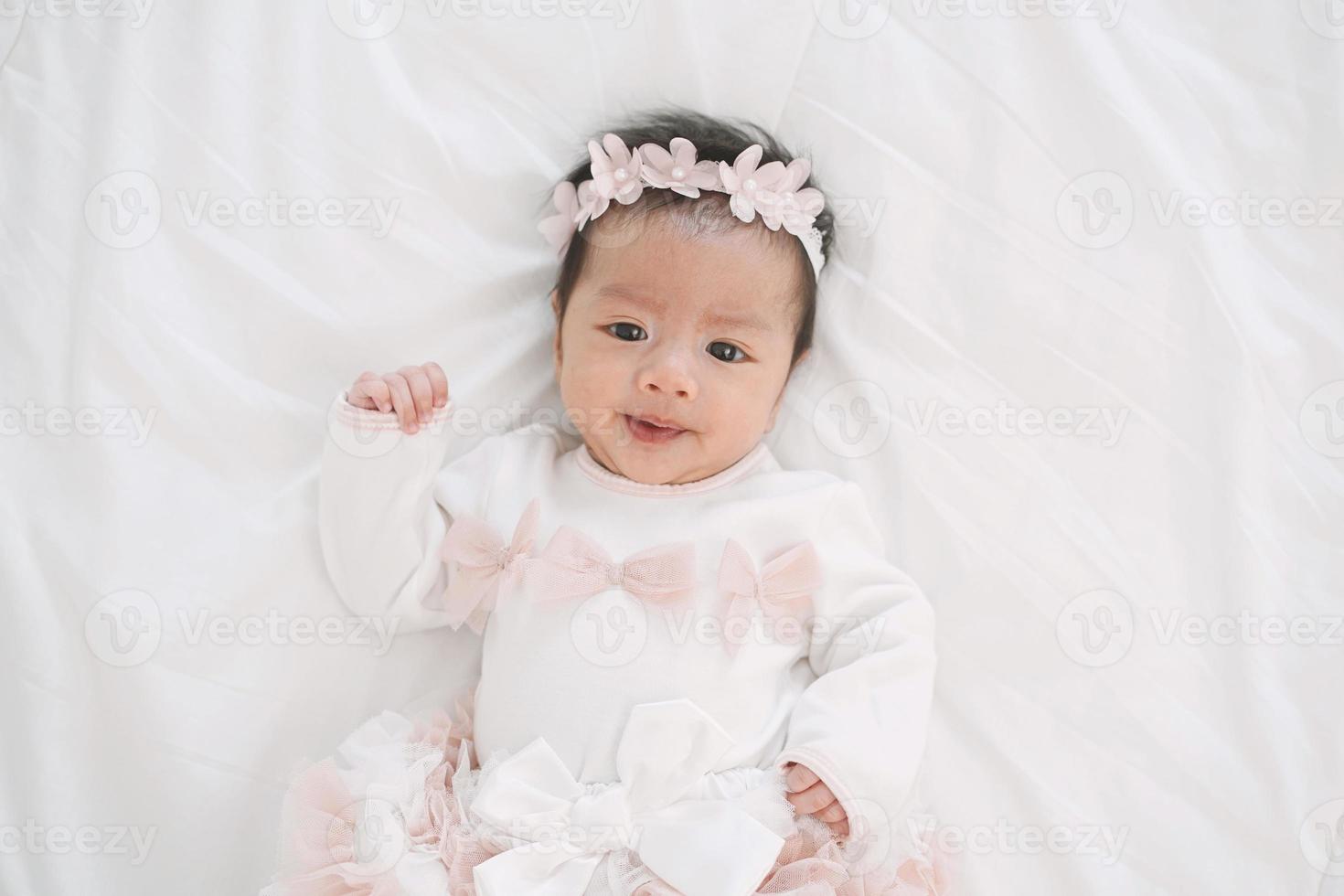Adorable little baby girl in a beautiful dress with flower band lying on a white blanket. photo