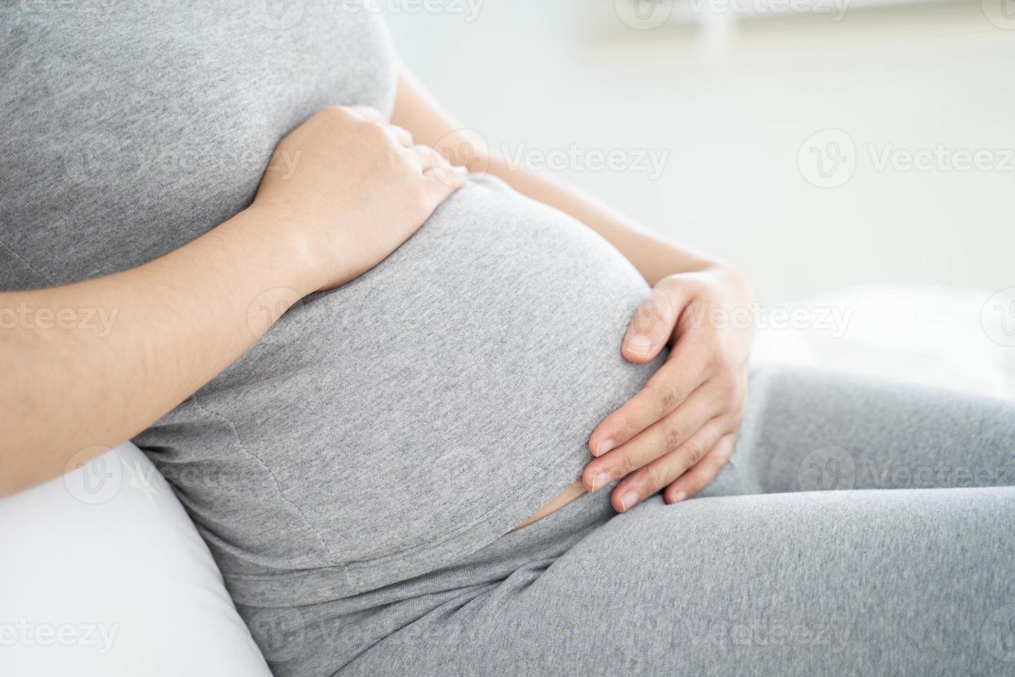 Close up of pregnant woman sitting on the bed and touching her belly at home. Selective focus. photo