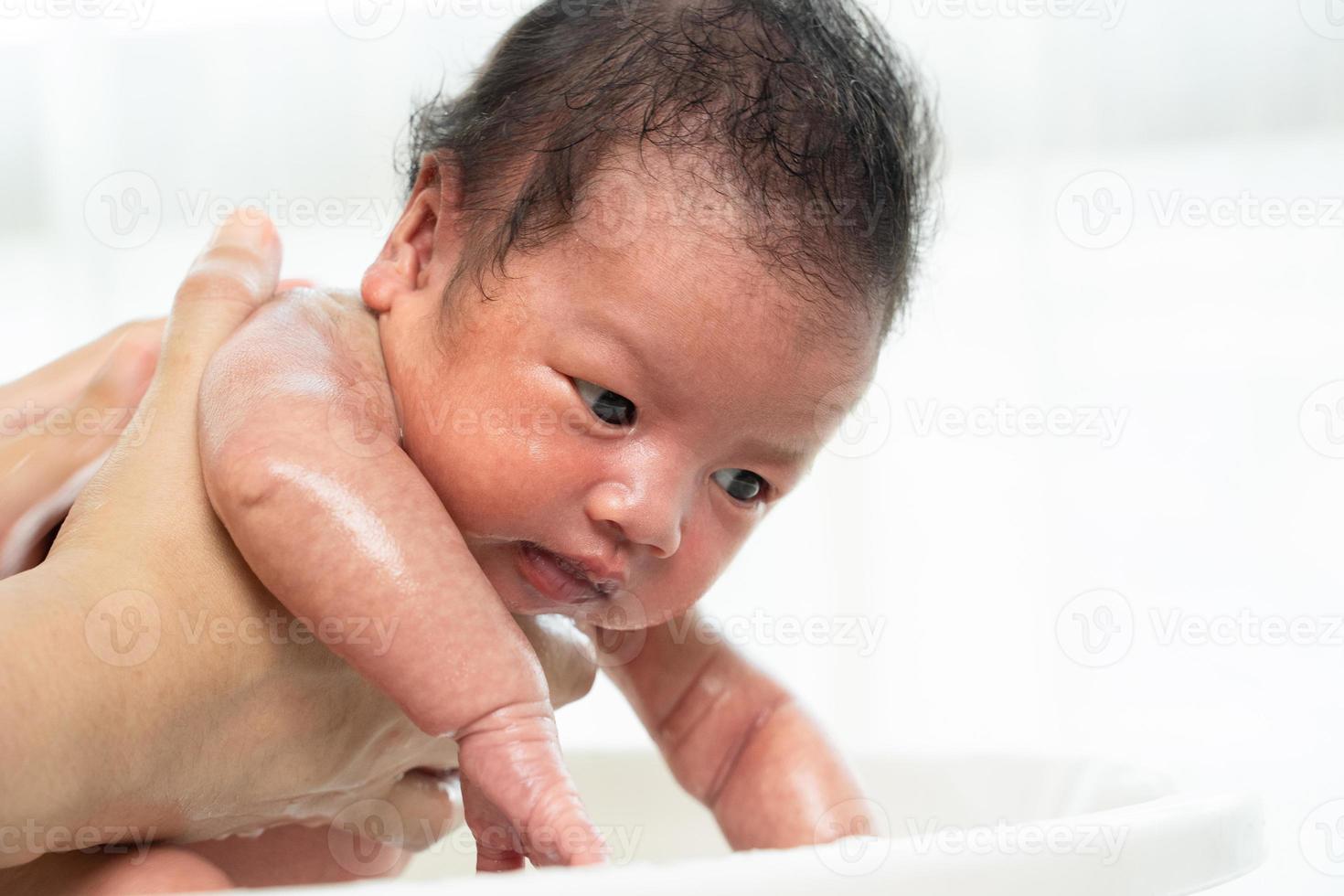 Newborn is being bathed by her mother using tub at home. photo