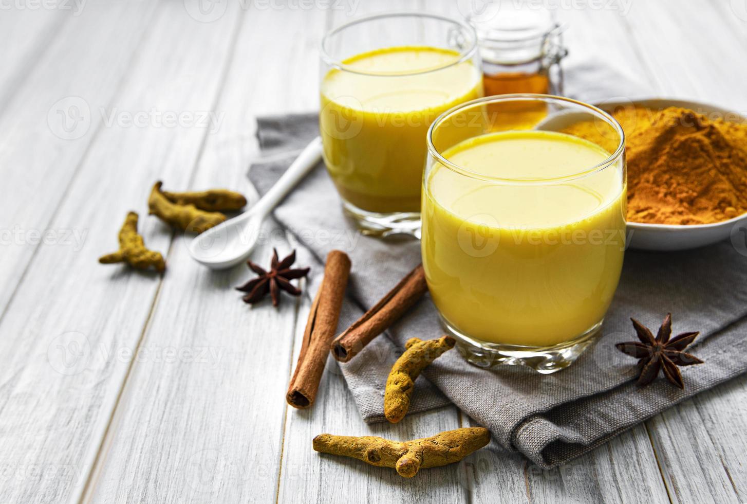 bebida latte de cúrcuma amarilla. Leche dorada con canela, cúrcuma, jengibre y miel sobre fondo de mármol blanco. foto