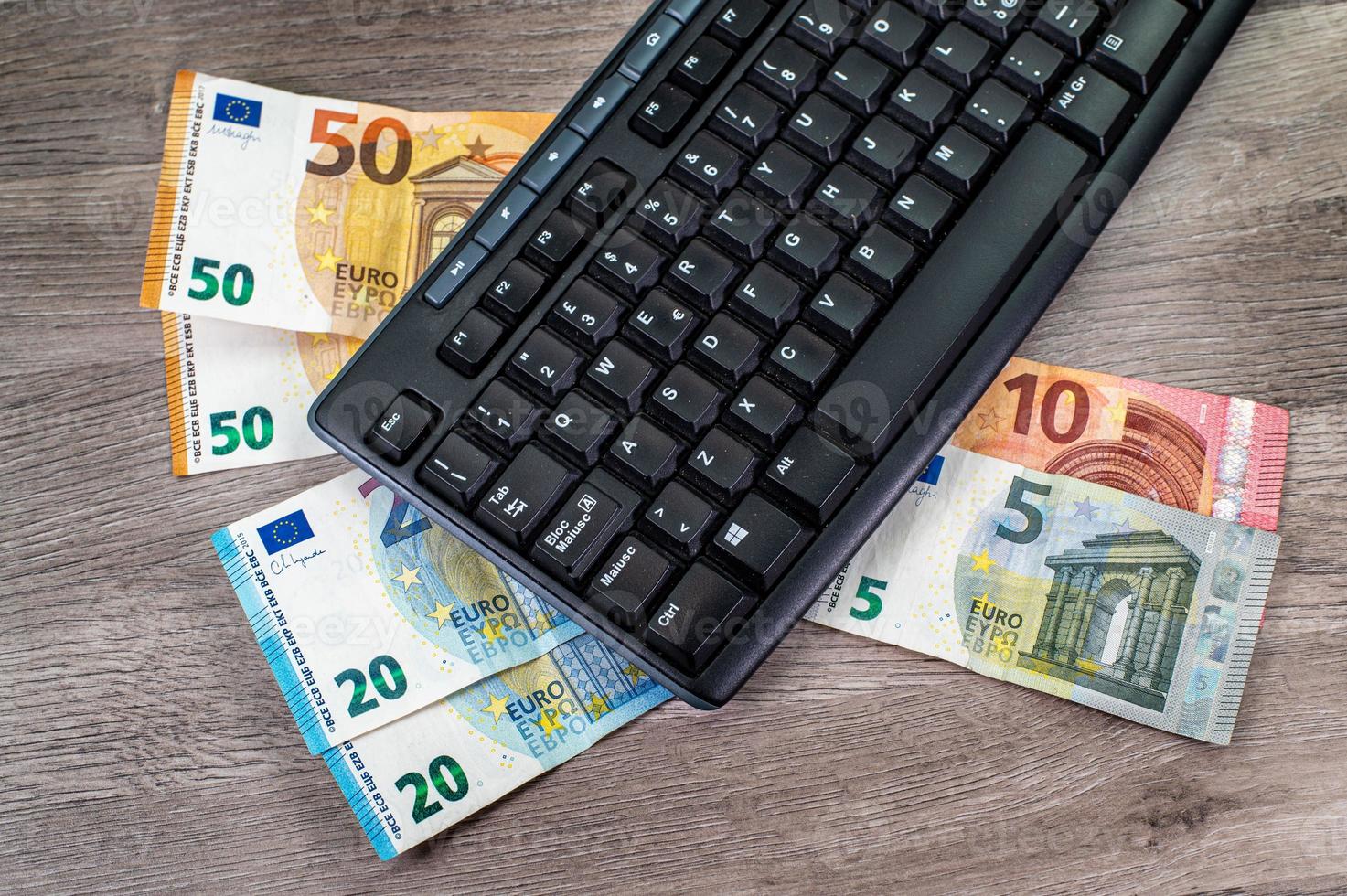 Billetes en euros de diferentes denominaciones y teclado de computadora sobre fondo de madera foto