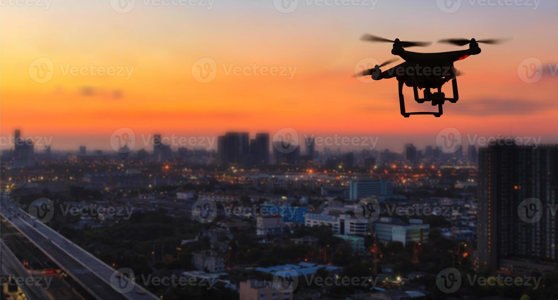 silueta de drone volando por encima de la ciudad al atardecer foto