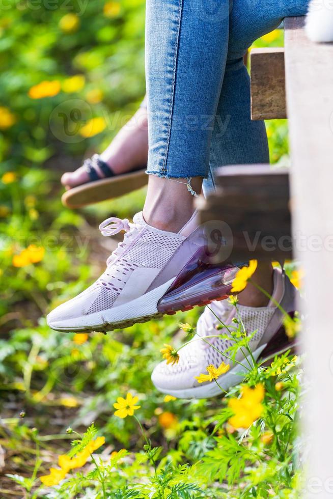 Mujer sentada en el puente de madera y piernas colgantes en el jardín de flores foto