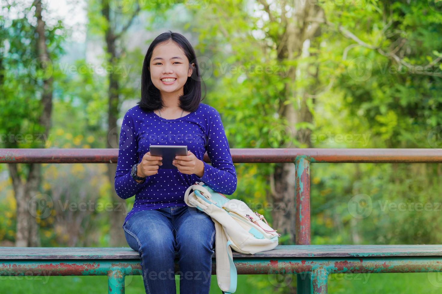 Asian student girl using a digital tablet in the park in a sunny summer day photo