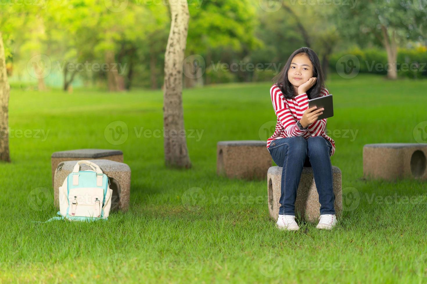 Chica estudiante asiática con una tableta digital en el parque escolar en un día soleado de verano foto
