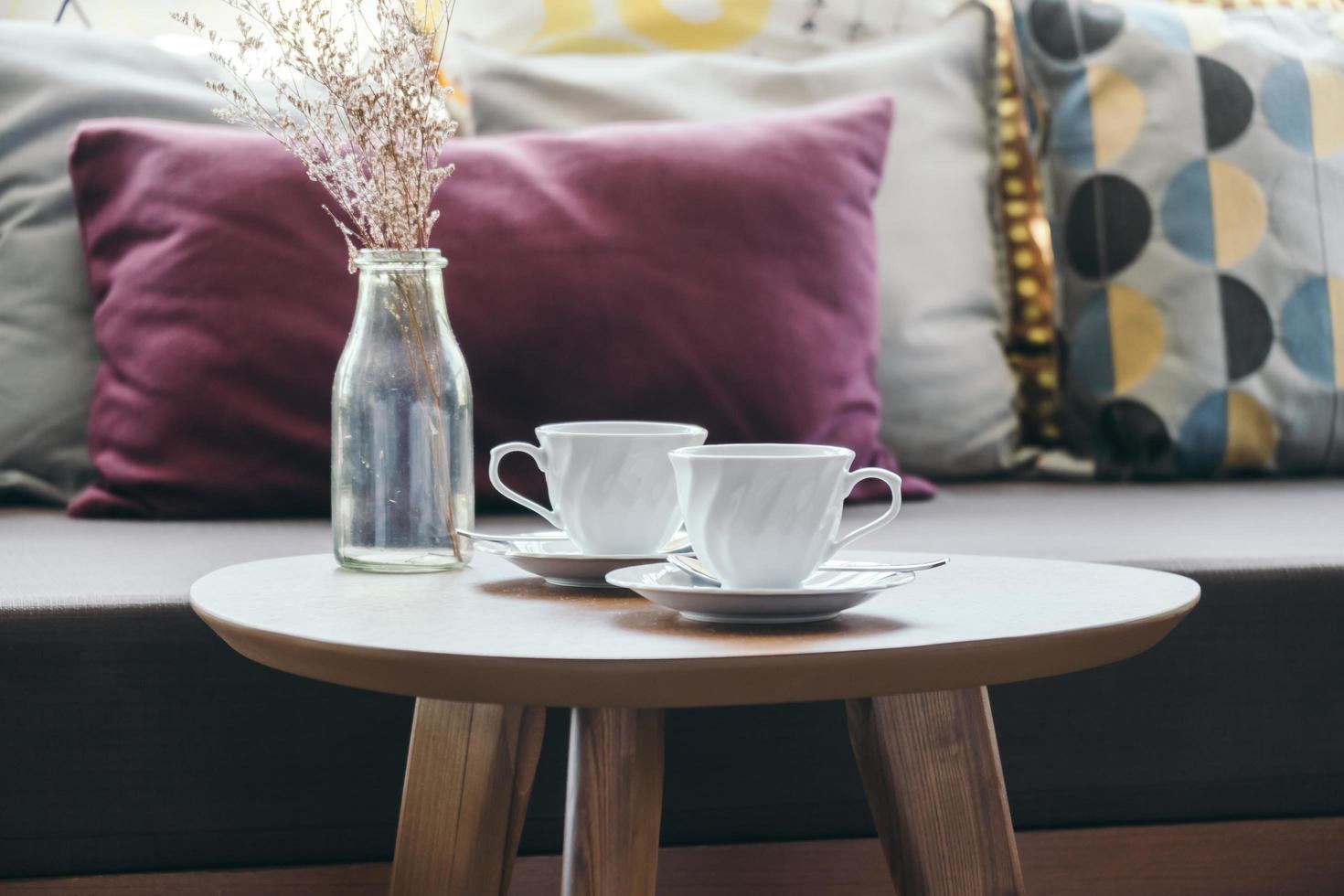 Taza de café con leche con jarrón de flores en la decoración de la mesa con una almohada en el sofá foto