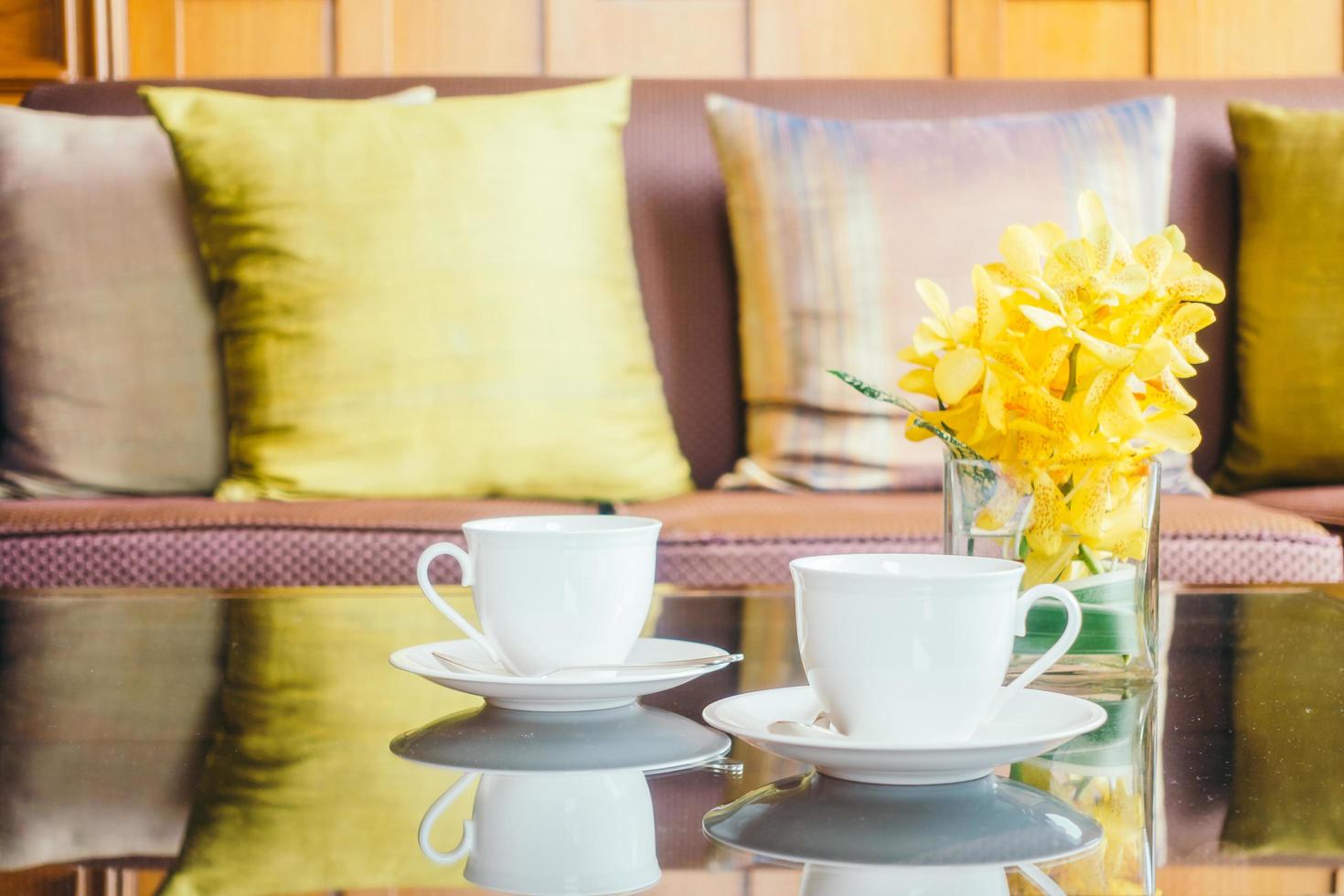 Florero de flores y taza de café con leche en la mesa y la almohada en el sofá foto