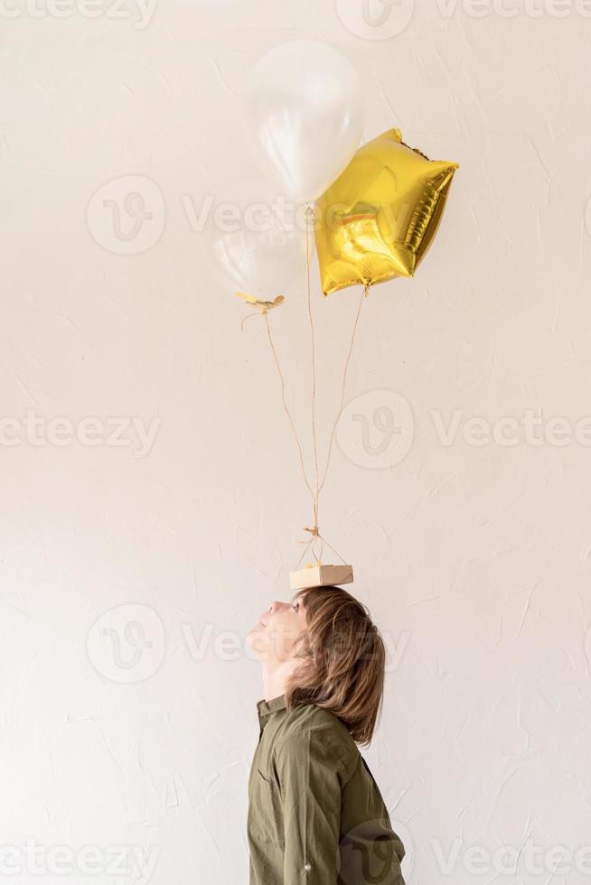 Chico divertido jugando con globos de helio, sosteniéndolos en la cabeza. foto
