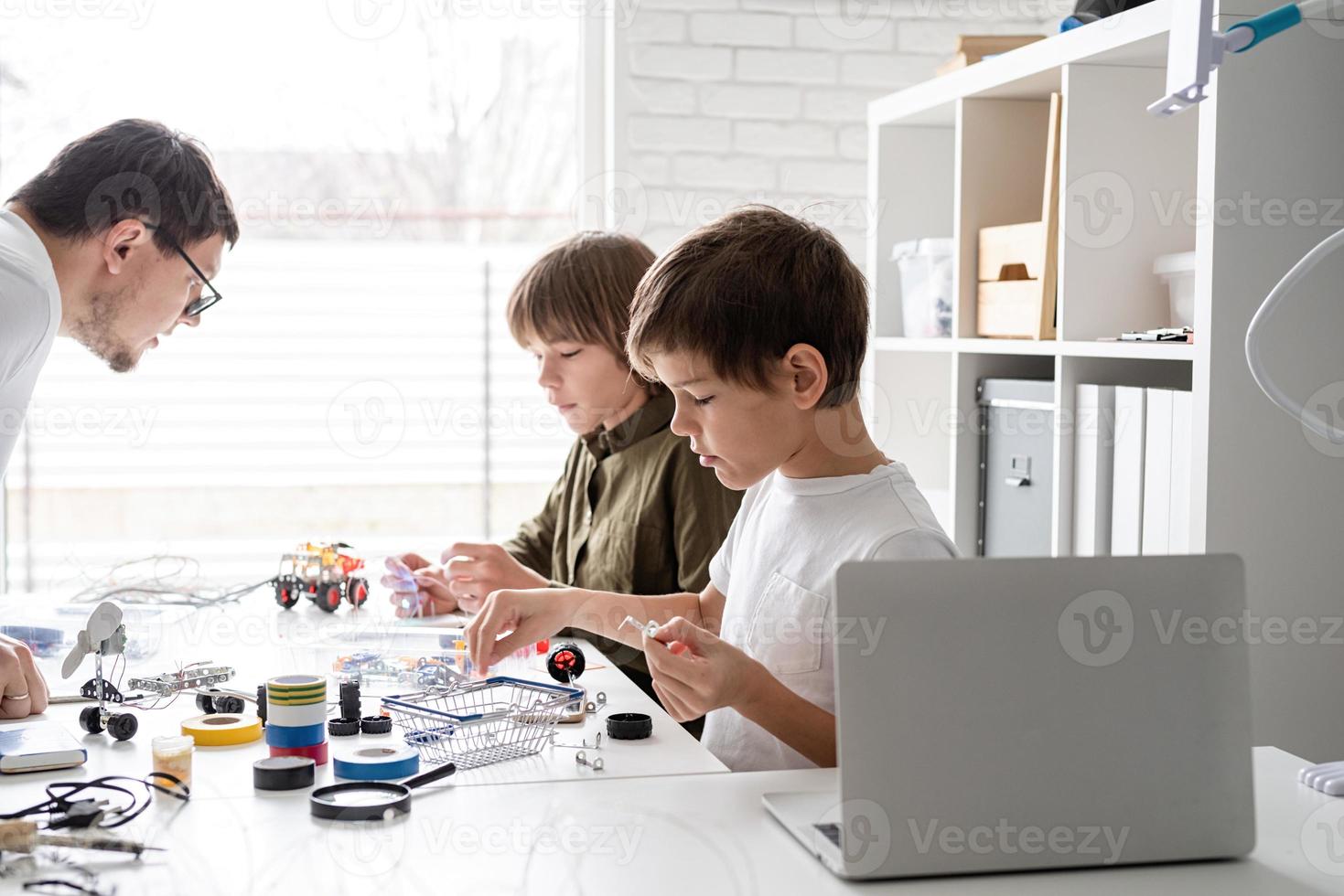 Young boys and teacher having fun constructing robot cars at the workshop photo