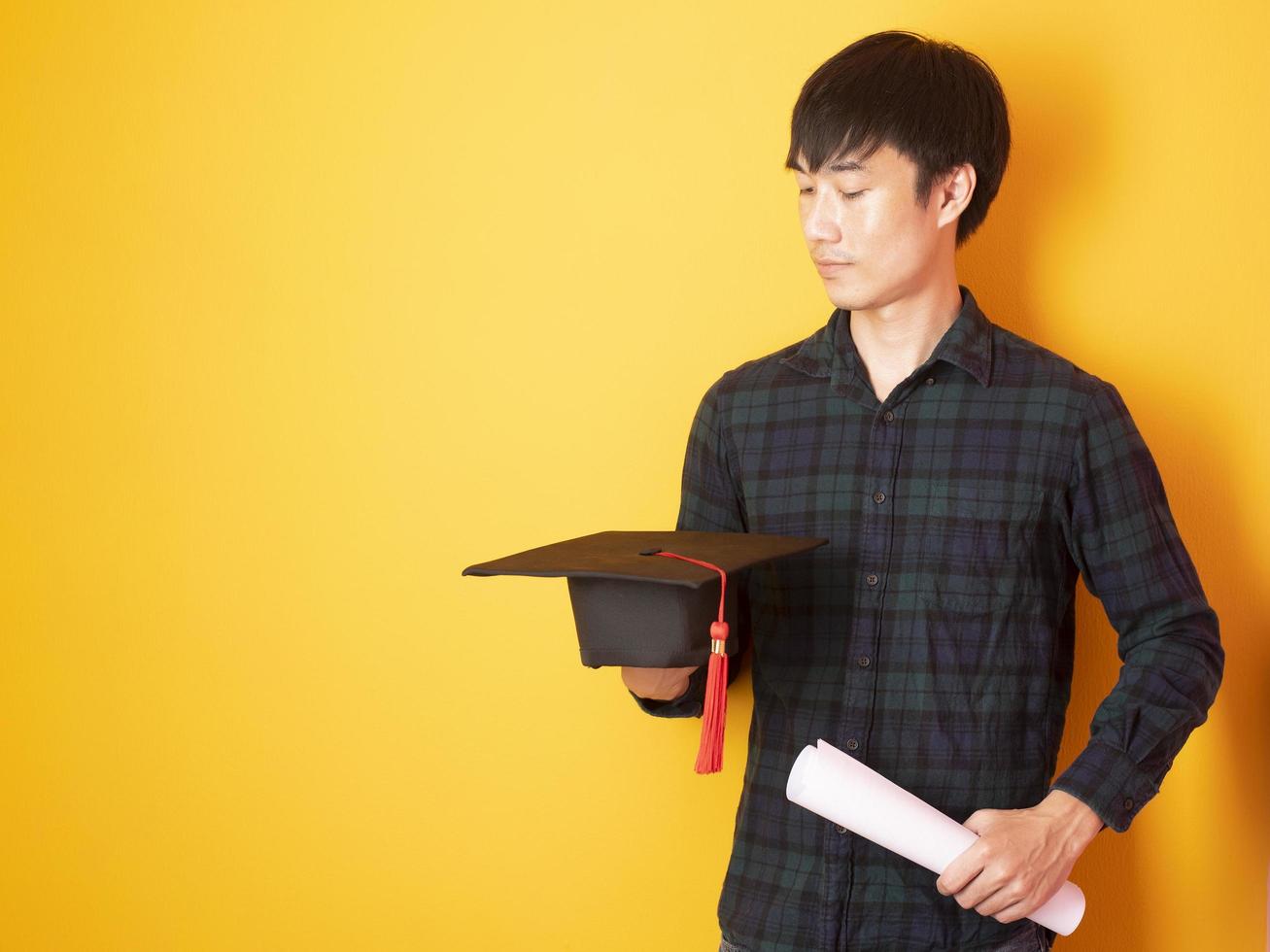 El hombre universitario está contento con la graduación sobre fondo amarillo foto