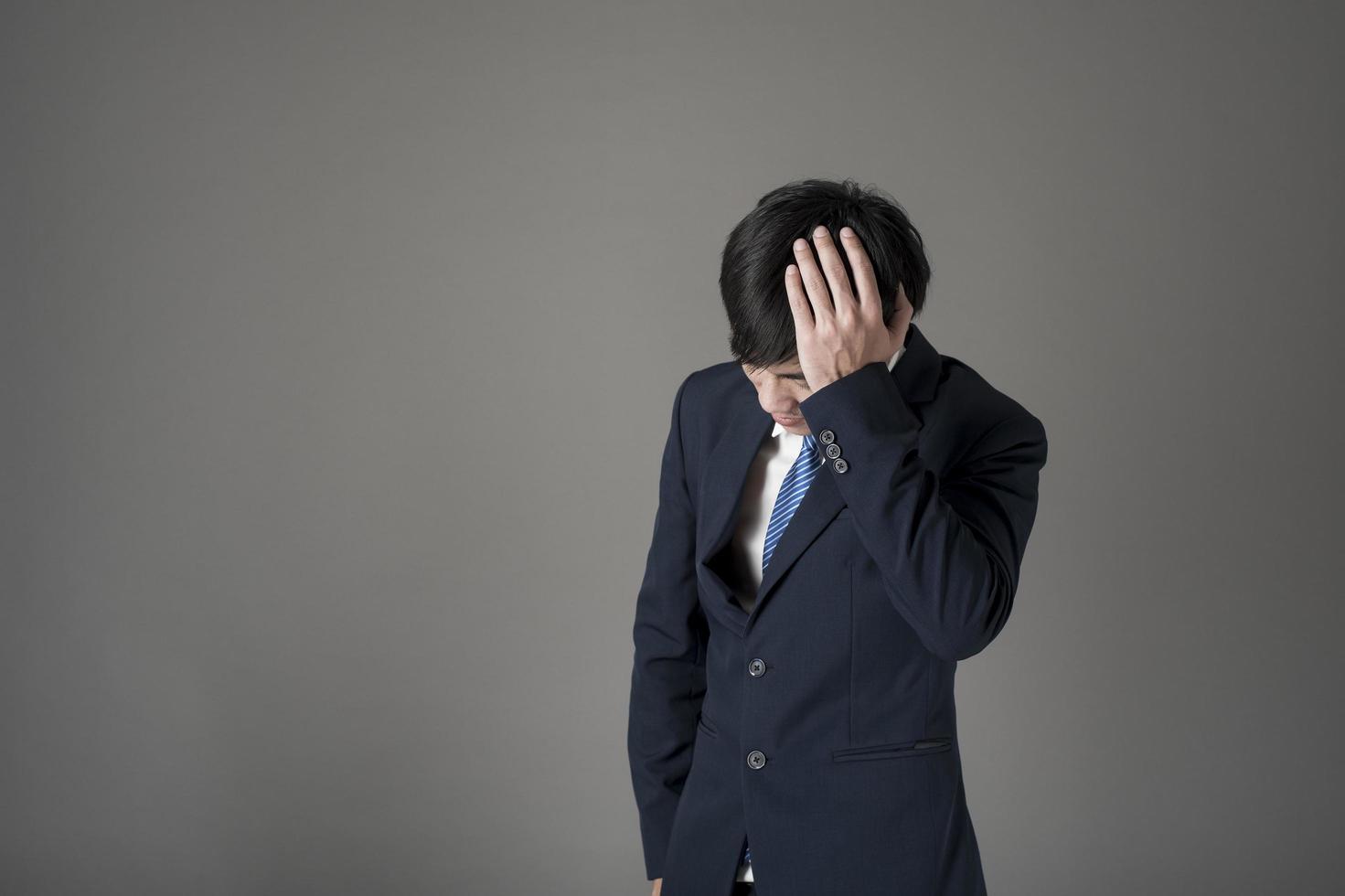 hombre de negocios es dolor de cabeza, fondo gris en estudio foto