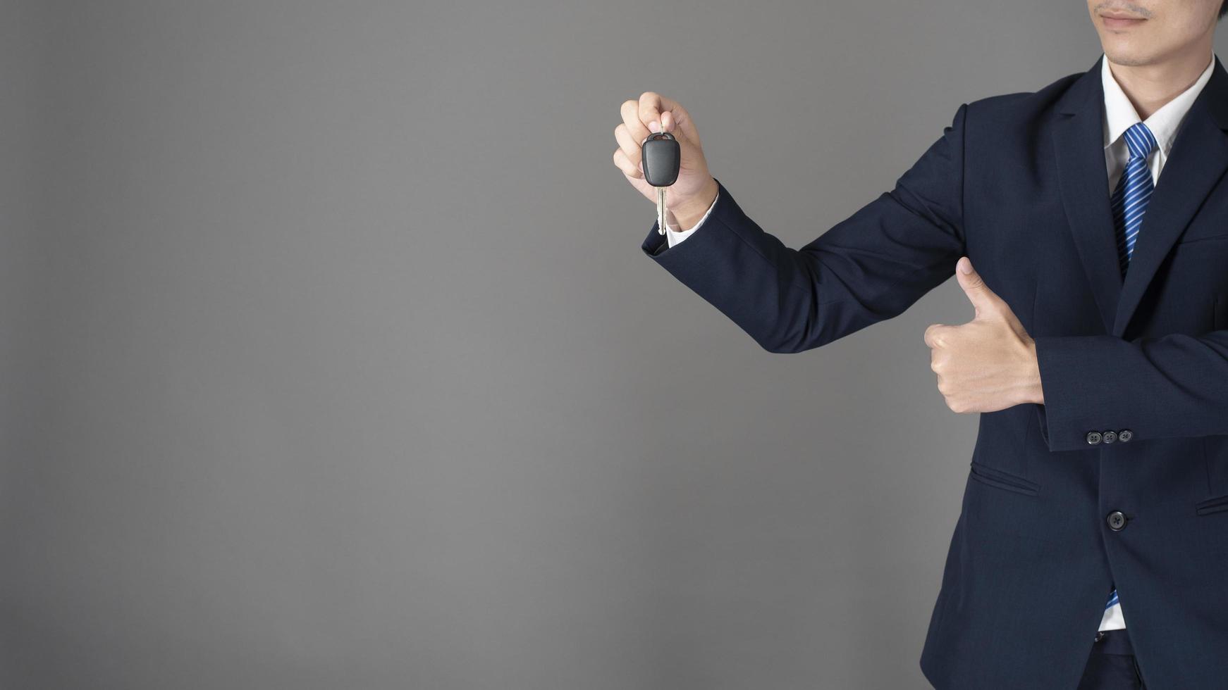 Business man is holding car key, grey background in studio photo