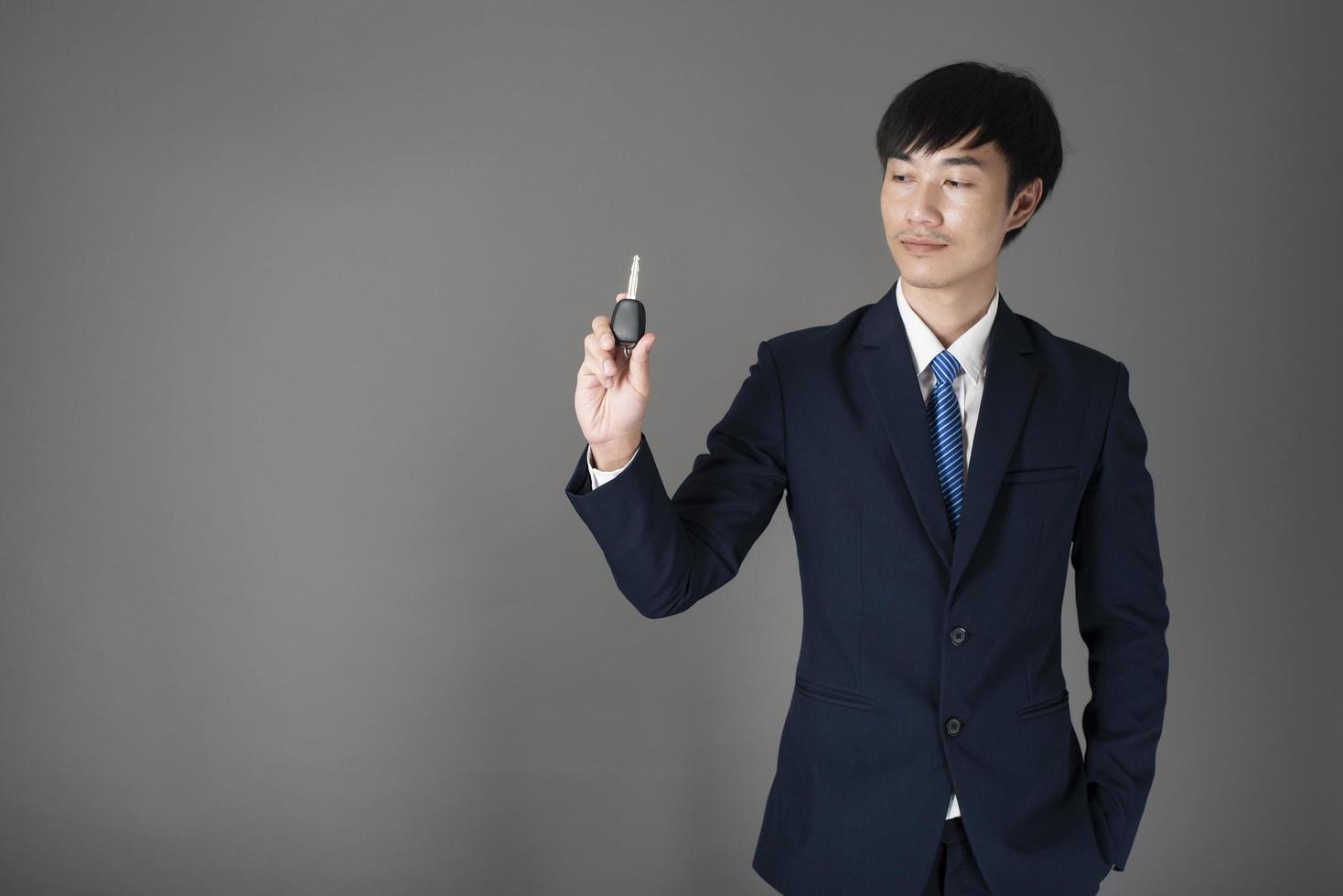 Business man is holding car key, grey background in studio photo