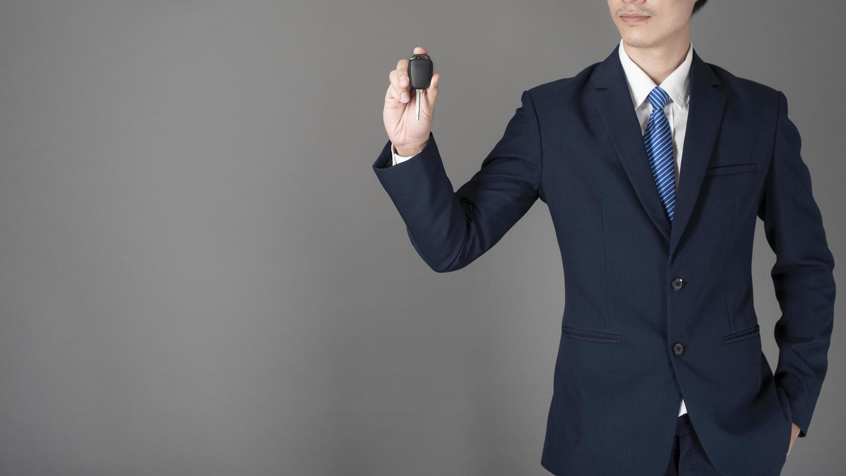 Business man is holding car key, grey background in studio photo