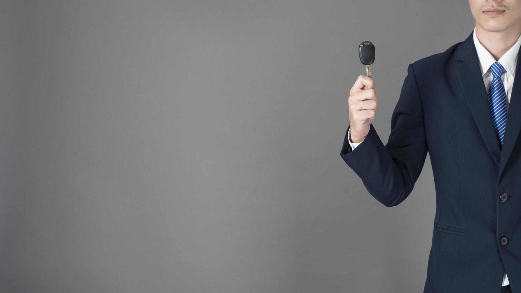 Business man is holding car key, grey background in studio photo