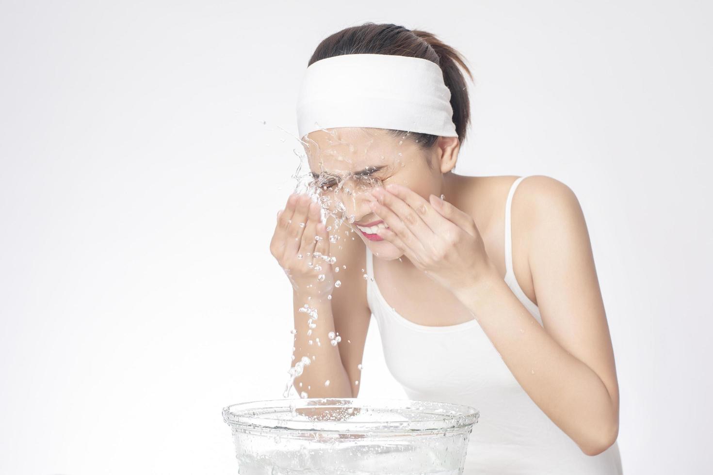 Beautiful woman is washing her face on white background photo