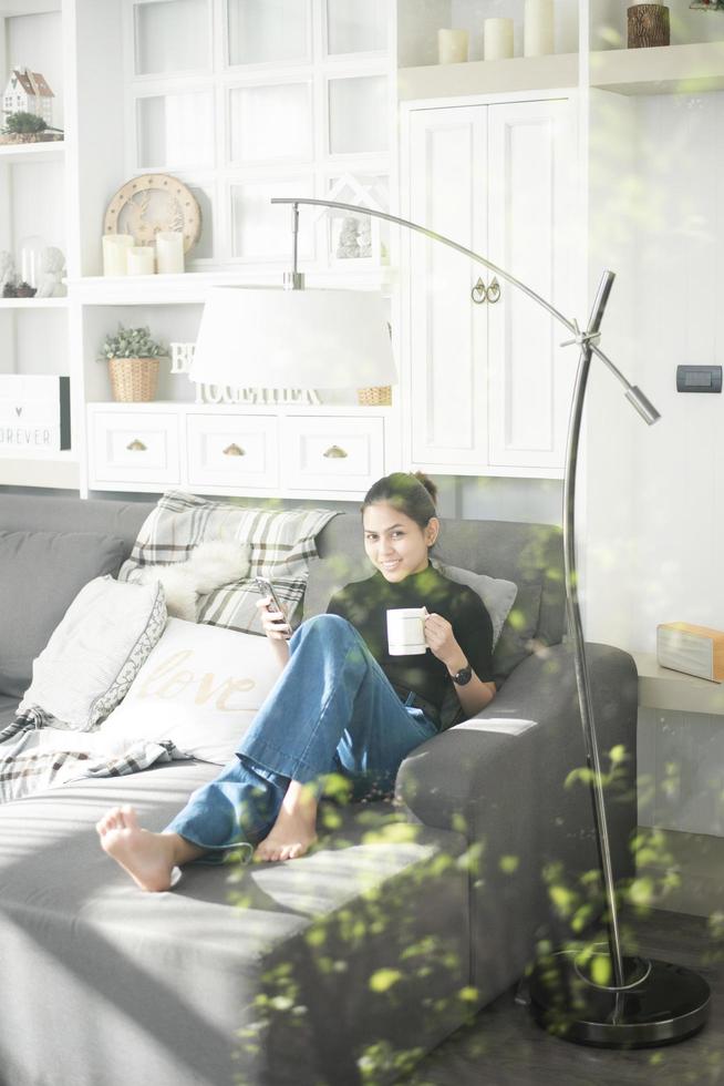 Hermosa mujer joven relajándose en el sofá en casa y usando teléfonos inteligentes. foto