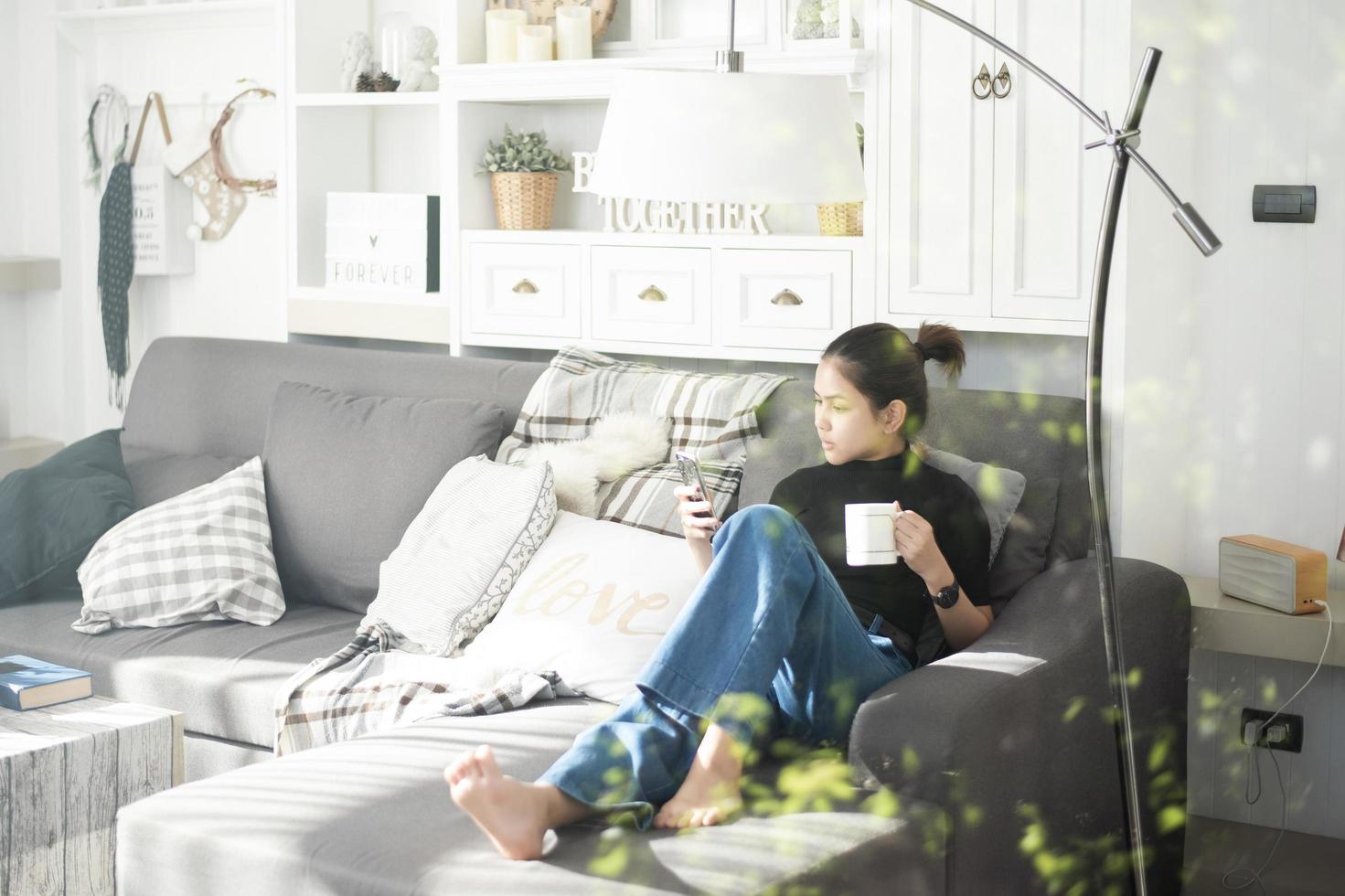 Hermosa mujer joven relajándose en el sofá en casa y usando teléfonos inteligentes. foto