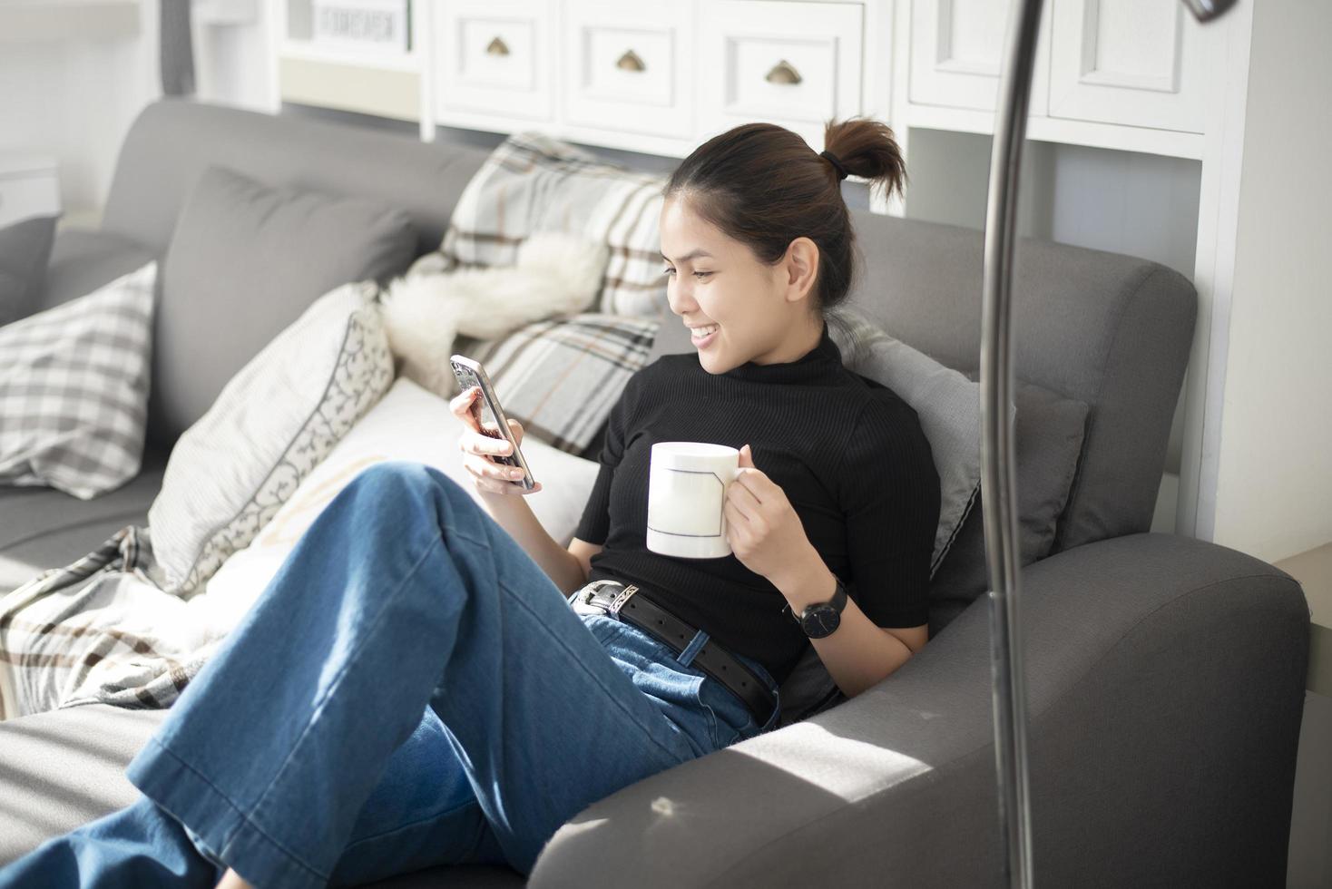 Hermosa mujer joven relajándose en el sofá en casa y usando teléfonos inteligentes. foto