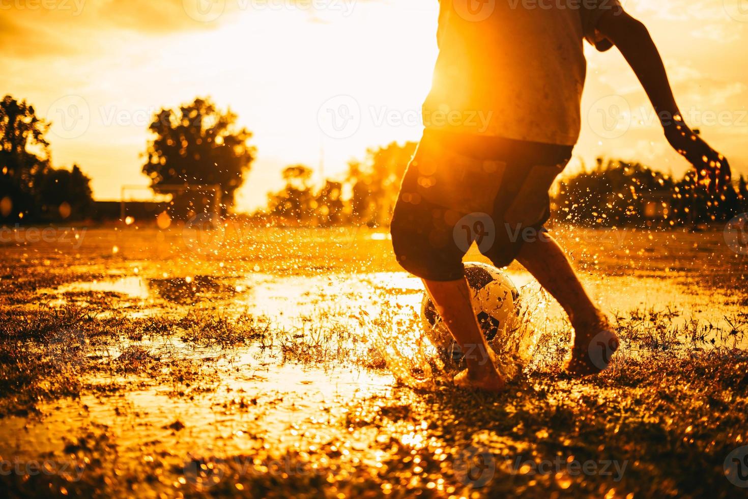 Imagen deportiva de acción de un grupo de niños jugando al fútbol para hacer ejercicio en una zona rural comunitaria bajo la lluvia foto